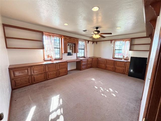 kitchen with built in desk, light colored carpet, a textured ceiling, and ceiling fan