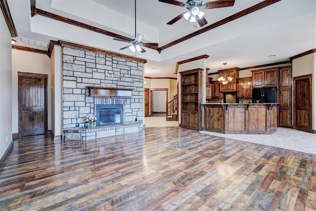 unfurnished living room featuring hardwood / wood-style floors, a stone fireplace, crown molding, and a tray ceiling