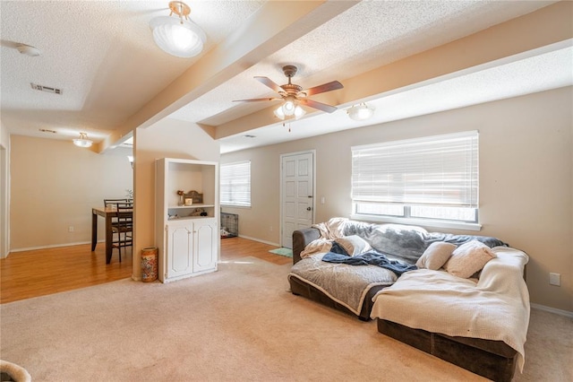 living room with a textured ceiling, light colored carpet, beam ceiling, and ceiling fan