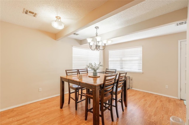 dining space featuring a textured ceiling, a chandelier, beamed ceiling, and light hardwood / wood-style flooring