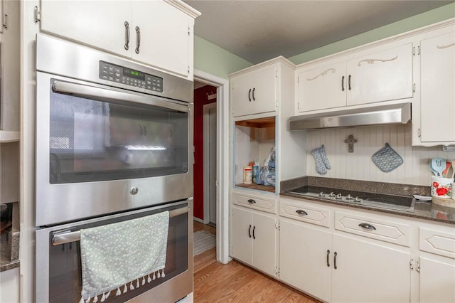 kitchen with white cabinetry, black stovetop, dark stone countertops, light hardwood / wood-style floors, and double oven