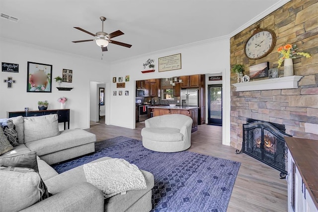 living room featuring ceiling fan, light hardwood / wood-style flooring, crown molding, and a stone fireplace