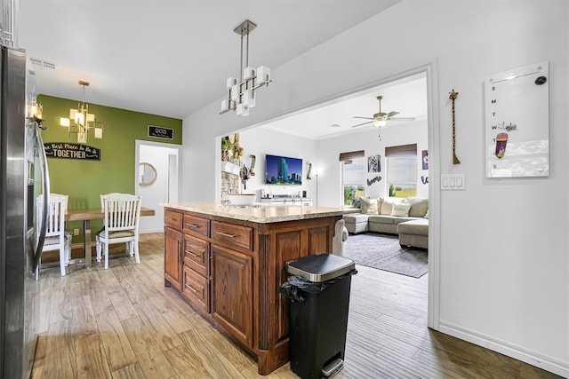 kitchen with pendant lighting, a kitchen island, light wood-type flooring, stainless steel fridge with ice dispenser, and ceiling fan with notable chandelier