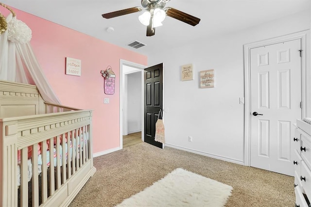 carpeted bedroom with ceiling fan and a crib