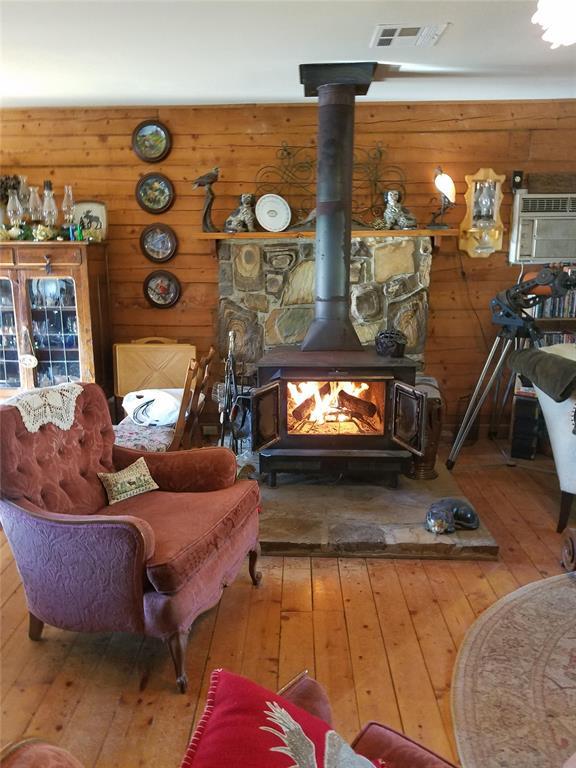 living area featuring wood walls, light wood-type flooring, an AC wall unit, and a wood stove