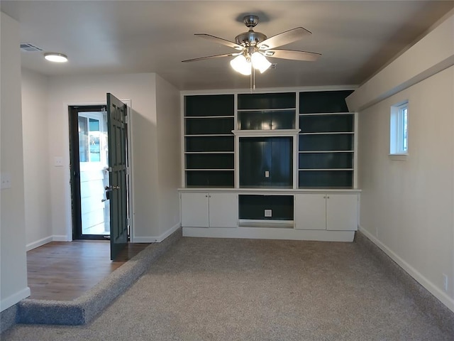 unfurnished living room with built in features, ceiling fan, and carpet flooring