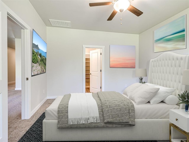 bedroom with a spacious closet, light colored carpet, a closet, and ceiling fan