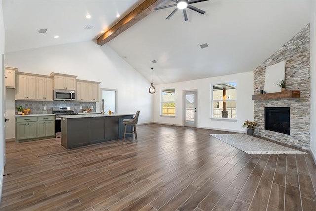 kitchen with stainless steel appliances, an island with sink, ceiling fan, a fireplace, and beam ceiling