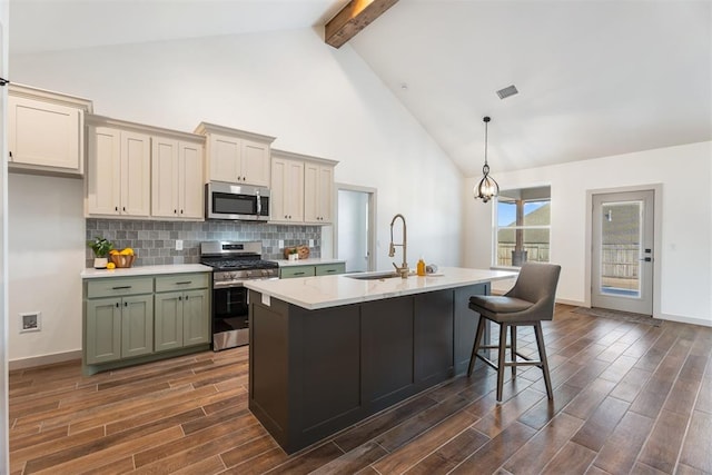 kitchen with stainless steel appliances, sink, decorative light fixtures, beamed ceiling, and a center island with sink