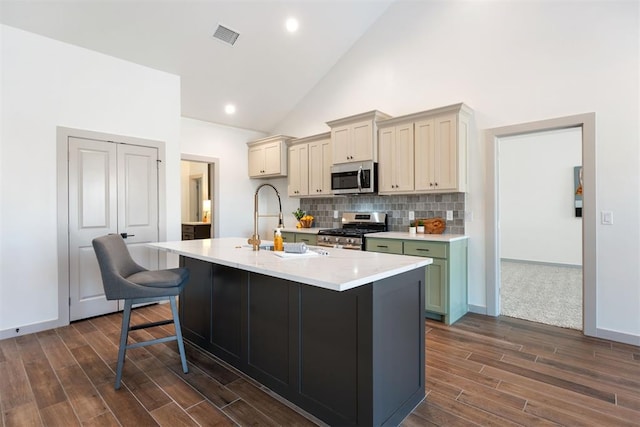 kitchen featuring an island with sink, high vaulted ceiling, backsplash, appliances with stainless steel finishes, and sink