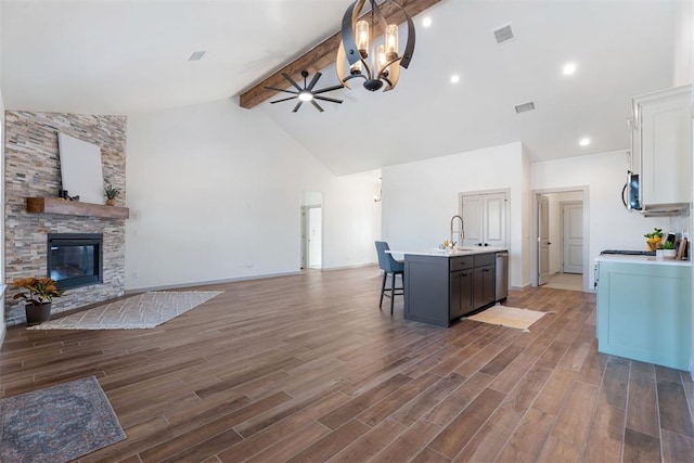 kitchen with white cabinets, a fireplace, pendant lighting, a kitchen island with sink, and beam ceiling