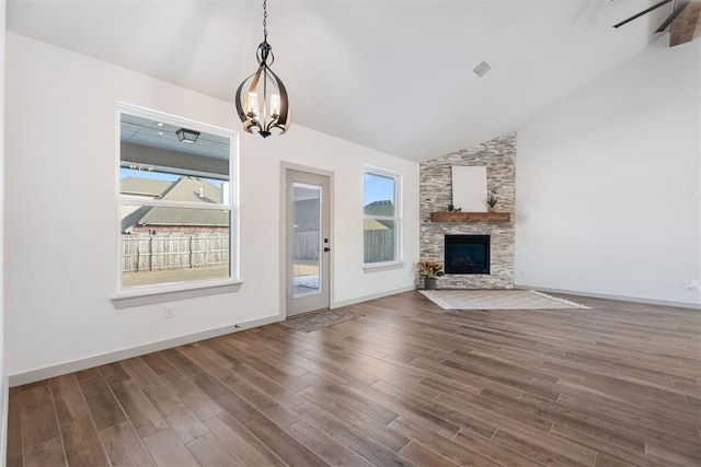 unfurnished living room with lofted ceiling, a stone fireplace, a notable chandelier, and dark hardwood / wood-style floors