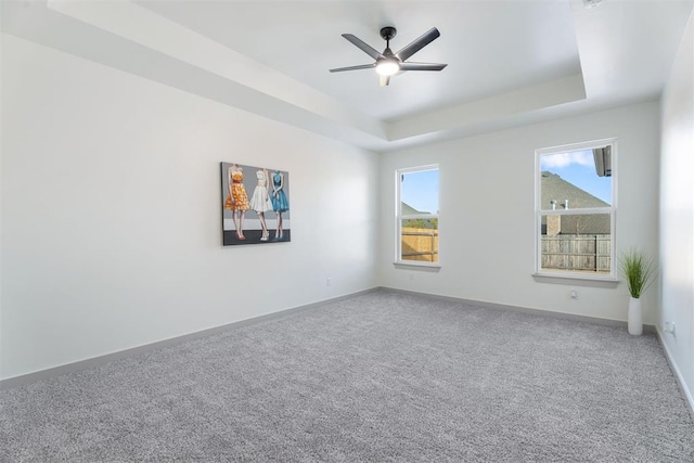 empty room featuring ceiling fan, a tray ceiling, and carpet