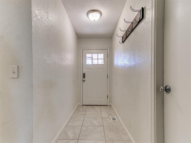 doorway with a textured ceiling and light tile patterned floors