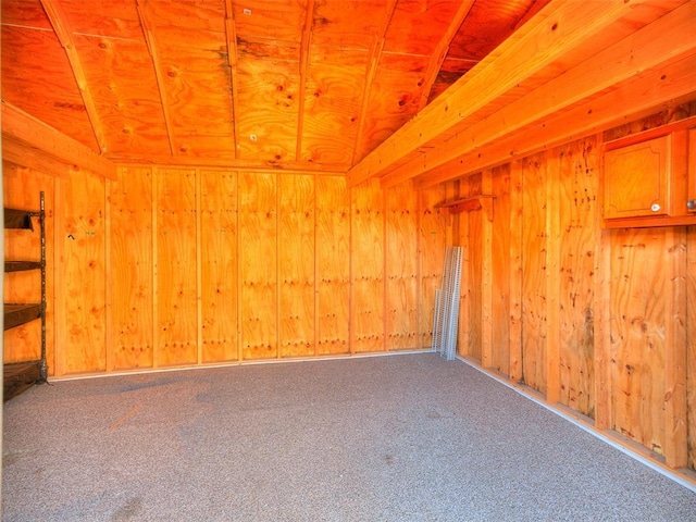 carpeted spare room with wood walls and vaulted ceiling