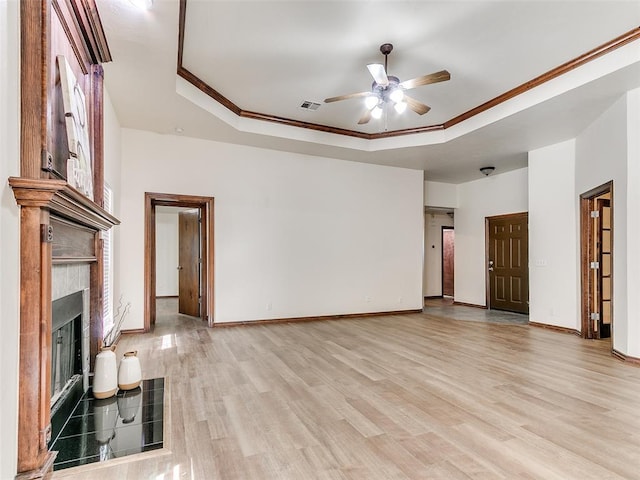 unfurnished living room with a tile fireplace, ceiling fan, ornamental molding, light hardwood / wood-style floors, and a tray ceiling