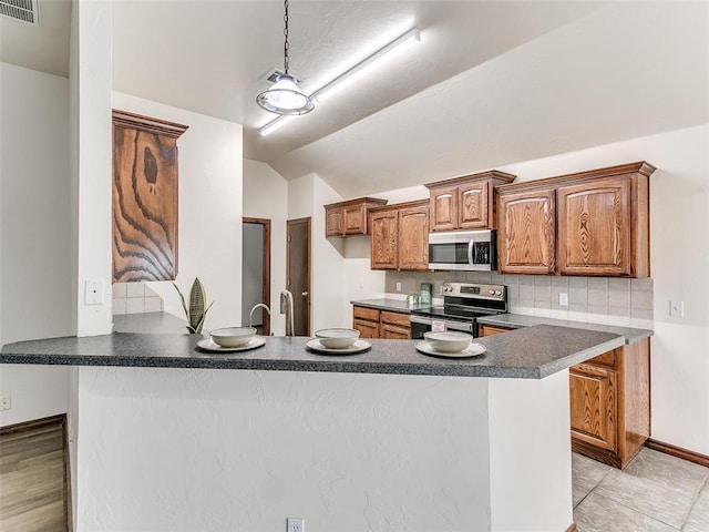 kitchen with kitchen peninsula, vaulted ceiling, decorative light fixtures, tasteful backsplash, and appliances with stainless steel finishes