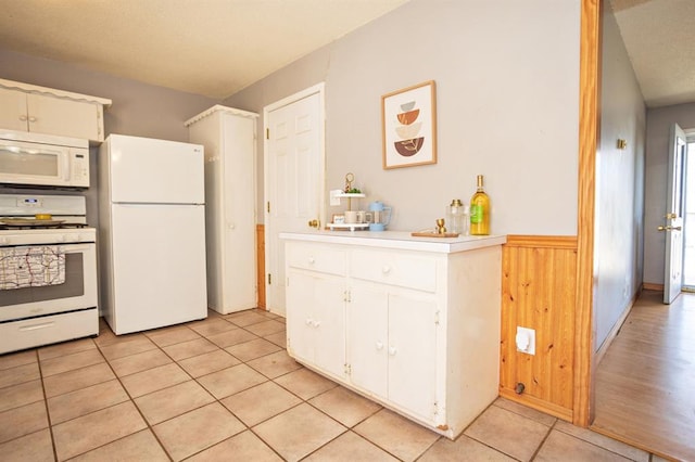 kitchen with white appliances, light tile patterned flooring, white cabinets, and wood walls