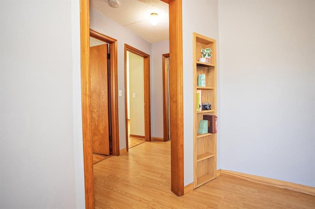 corridor with a textured ceiling, built in features, and light hardwood / wood-style flooring