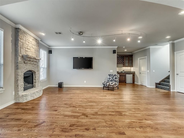 unfurnished living room with crown molding, wet bar, a fireplace, and light hardwood / wood-style flooring