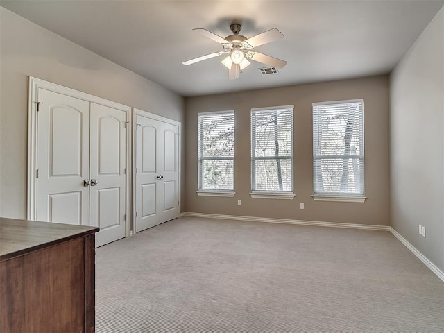 unfurnished bedroom with two closets, light colored carpet, and ceiling fan