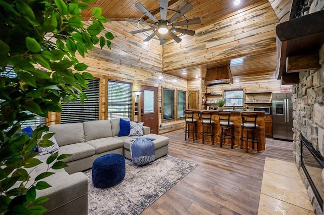 living room with light hardwood / wood-style floors, wooden walls, wood ceiling, high vaulted ceiling, and ceiling fan