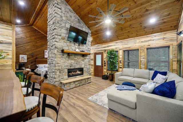 living room featuring a stone fireplace, wooden ceiling, wood walls, ceiling fan, and high vaulted ceiling