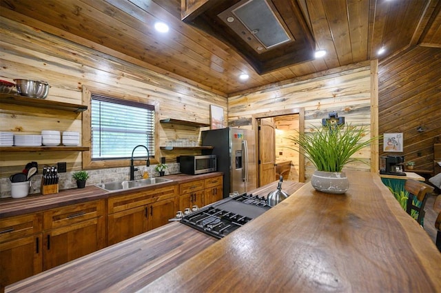 kitchen featuring stainless steel appliances, wood walls, wood ceiling, wooden counters, and sink