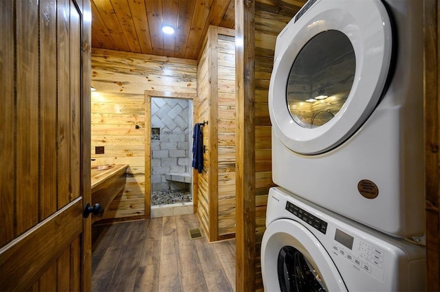 laundry area with wood walls, dark hardwood / wood-style floors, wood ceiling, and stacked washer / drying machine