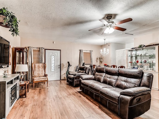 living room with ceiling fan with notable chandelier, a textured ceiling, and light hardwood / wood-style flooring