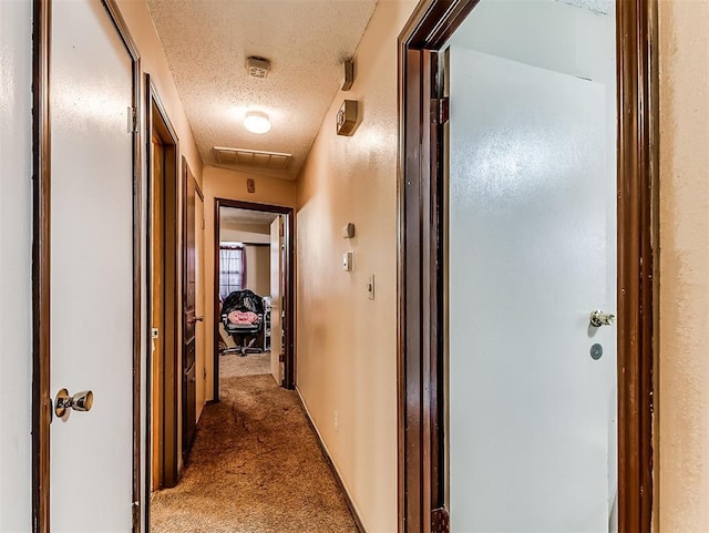 hallway with dark carpet and a textured ceiling