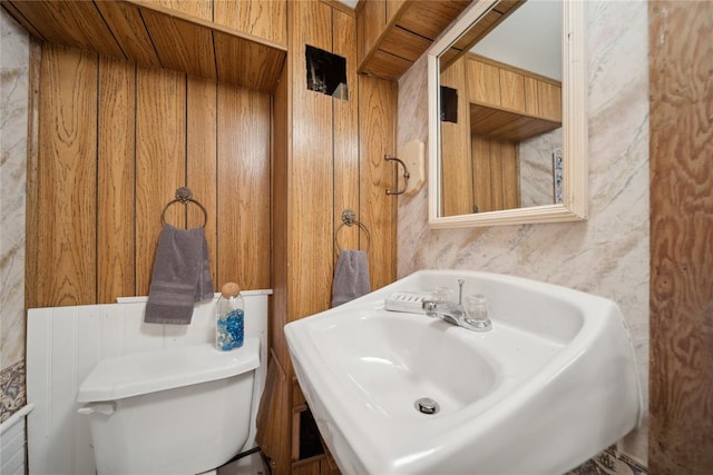 bathroom with sink, toilet, and wood walls