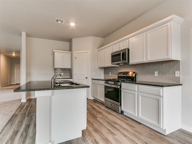 13156 Mannington Rd, Edmond, OK 73025 - kitchen featuring appliances with stainless steel finishes, a sink, light wood-style flooring, decorative backsplash, and white cabinetry