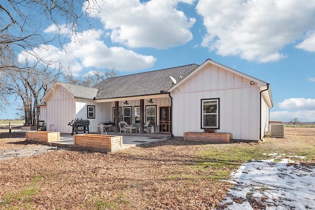 rear view of house with a patio, board and batten siding, cooling unit, and roof with shingles