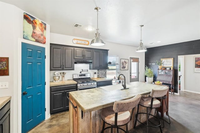 kitchen with under cabinet range hood, a sink, visible vents, stainless steel gas range, and finished concrete floors