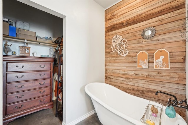 full bath featuring a freestanding bath, concrete floors, baseboards, and wooden walls