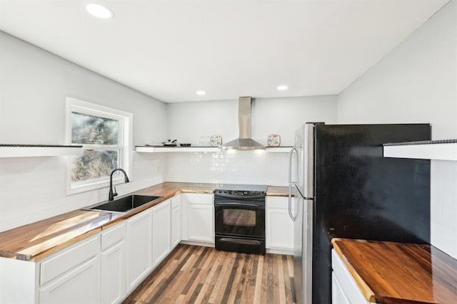 kitchen with wooden counters, electric range, freestanding refrigerator, a sink, and wall chimney exhaust hood