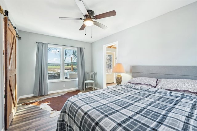 bedroom with a barn door, baseboards, ceiling fan, and wood finished floors