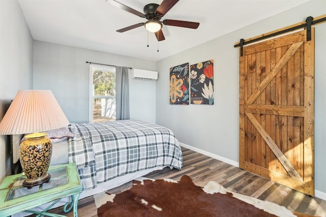 bedroom featuring a barn door, baseboards, a ceiling fan, wood finished floors, and a wall mounted AC