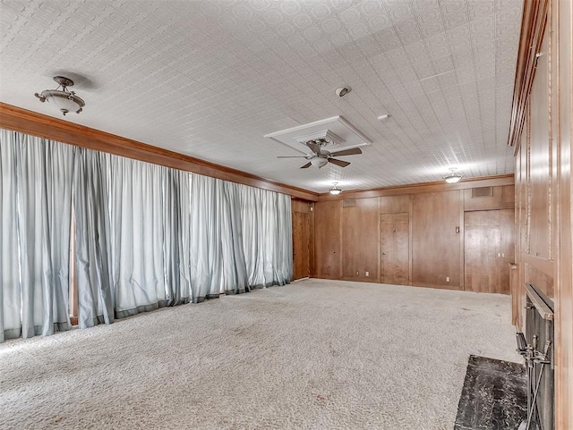 empty room featuring ceiling fan, a premium fireplace, carpet floors, wood walls, and crown molding