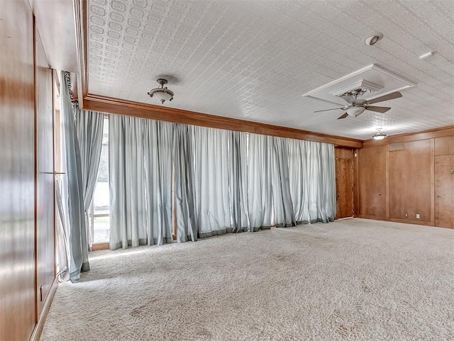 interior space with wooden walls, carpet flooring, ceiling fan, and crown molding