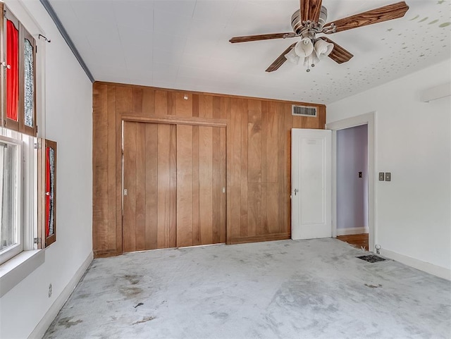 unfurnished bedroom with wooden walls, a closet, ceiling fan, and light colored carpet