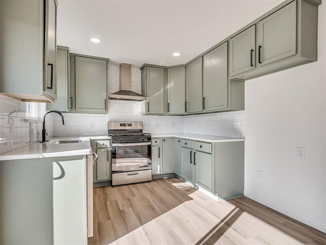 kitchen featuring sink, light wood-type flooring, decorative backsplash, gas stove, and wall chimney range hood