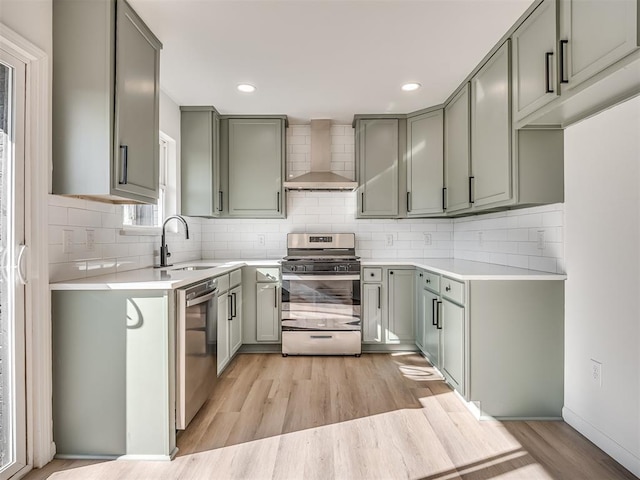 kitchen with appliances with stainless steel finishes, light wood-type flooring, wall chimney exhaust hood, sink, and backsplash