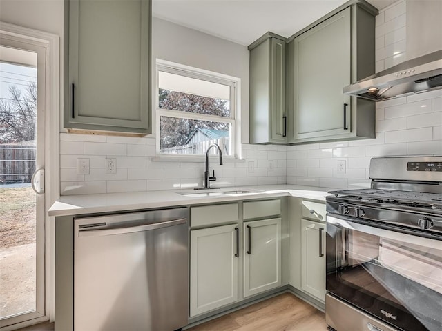 kitchen with light hardwood / wood-style flooring, stainless steel appliances, wall chimney range hood, green cabinetry, and sink