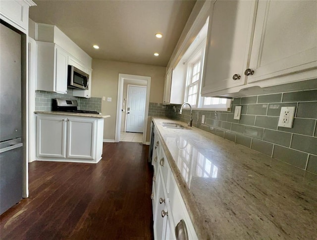 kitchen with sink, appliances with stainless steel finishes, white cabinets, light stone counters, and dark wood-type flooring