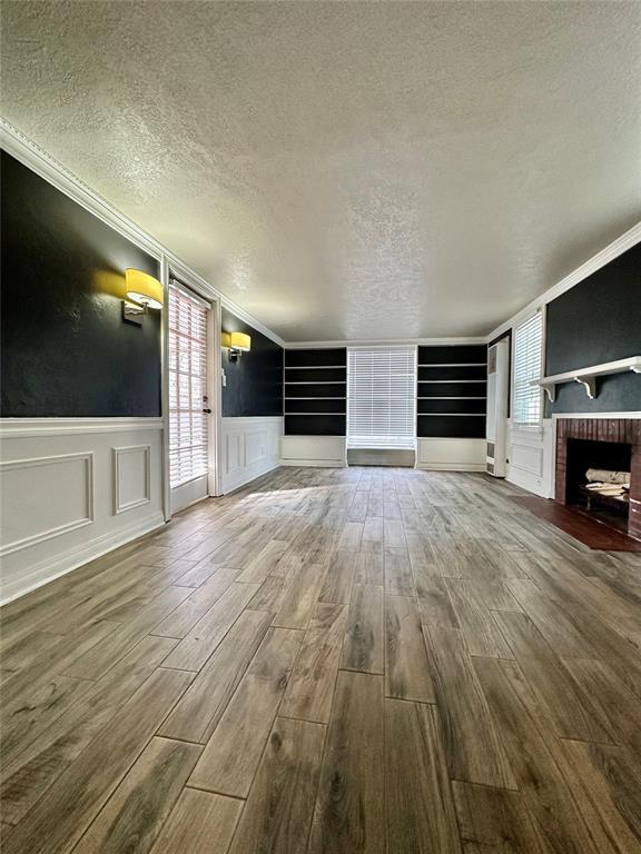 unfurnished living room featuring ornamental molding, a brick fireplace, a textured ceiling, and built in shelves