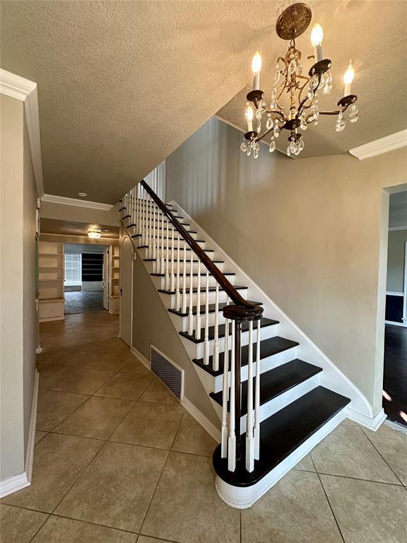 stairs with tile patterned flooring, a textured ceiling, crown molding, and a chandelier