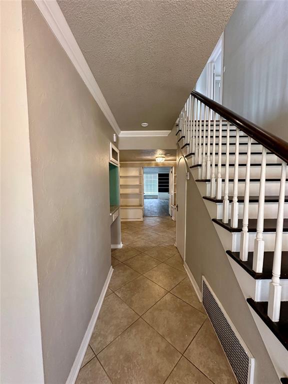 stairs with tile patterned flooring, a textured ceiling, and ornamental molding