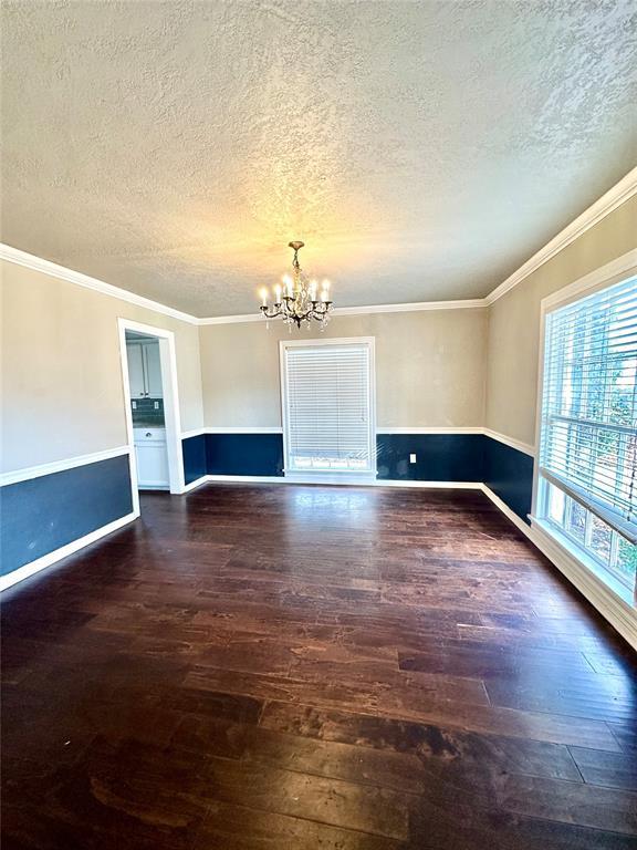 empty room featuring a textured ceiling, dark hardwood / wood-style flooring, ornamental molding, and a chandelier